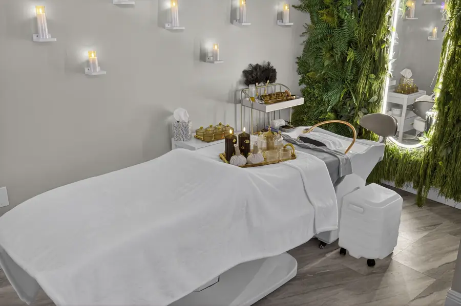 A white treatment bed in a suite lined with dozens of wall-mounted candle sconces beside a green living wall