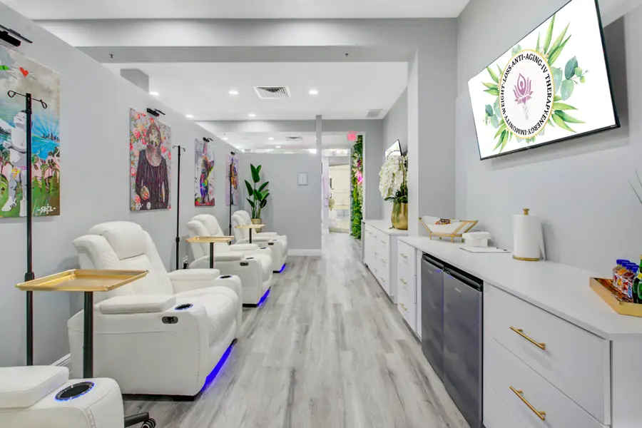 A long row of white leather IV recliners with violet LED underlighting running down the drip lounge toward the treatment area