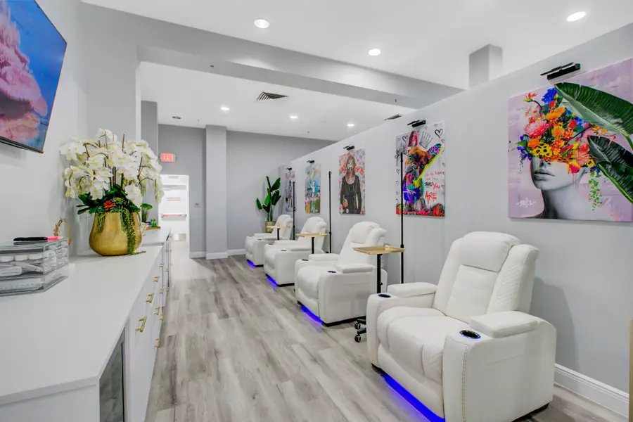 White IV recliners with violet LED underlighting beside a counter of white orchids and bright framed artwork