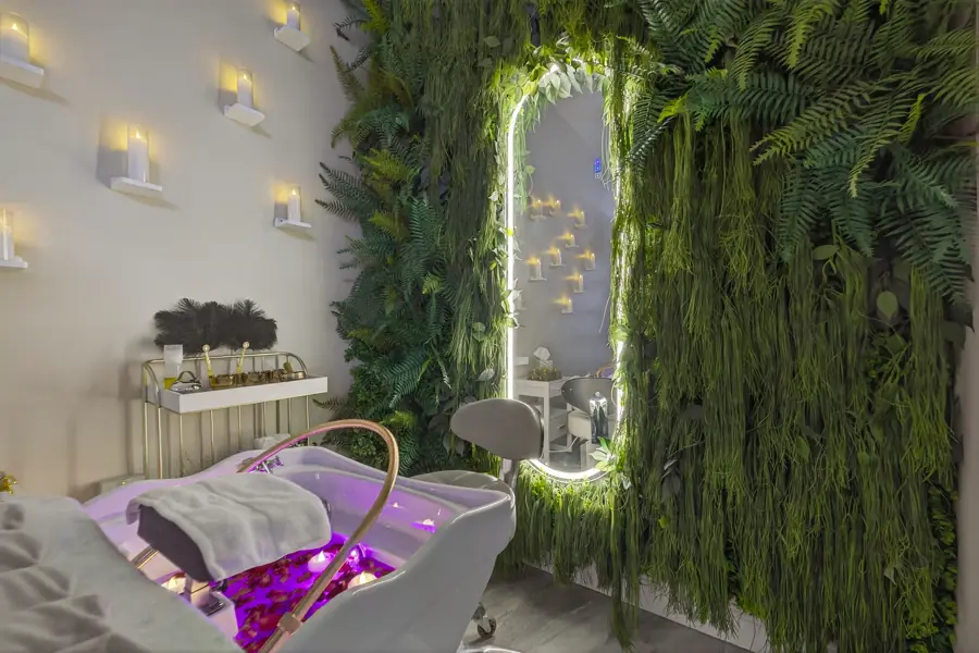 A head-spa treatment bed strewn with purple petals beside an illuminated arched mirror set into a fern-covered living wall
