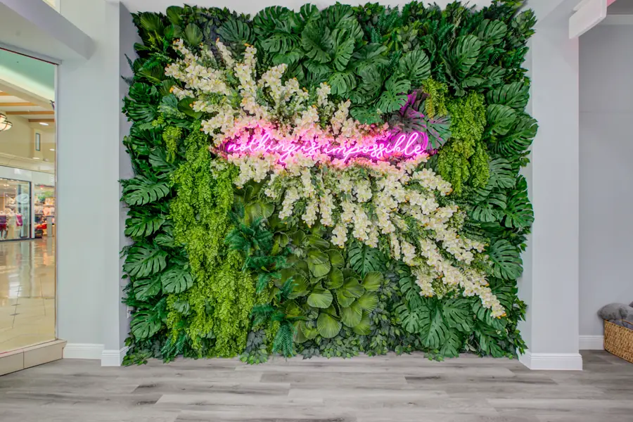 A dense preserved-moss and monstera living wall with a pink neon script sign glowing across it, in the Optimal Wellness lobby