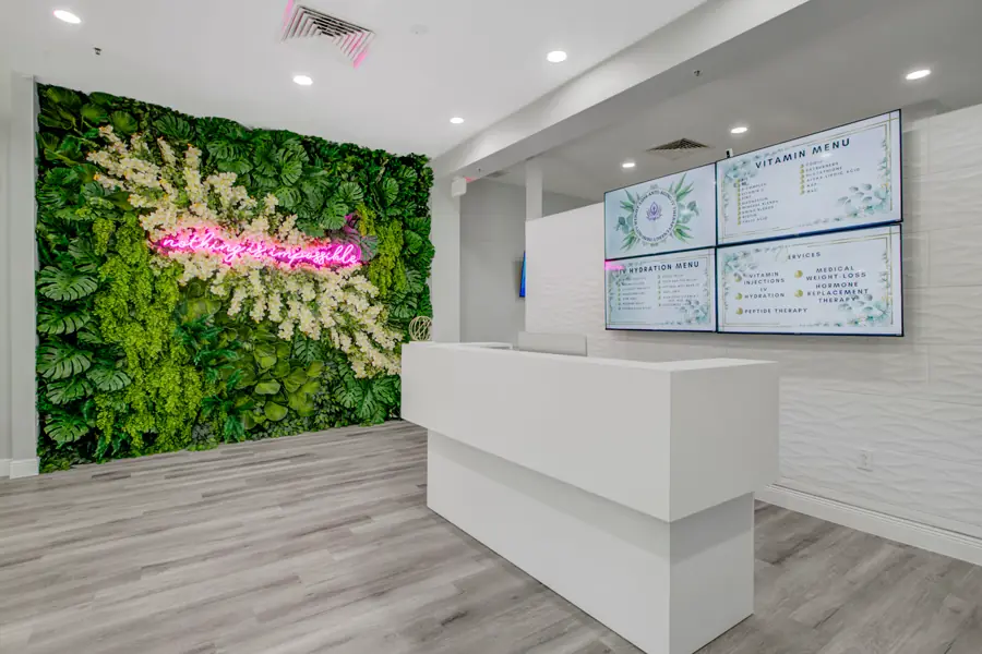 The white reception desk in front of a preserved living wall and pink neon script, with service menus on wall-mounted screens