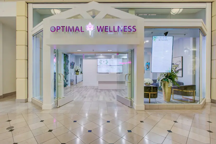 The Optimal Wellness mall storefront — a white arched entrance with glass walls opening onto the lobby and living wall
